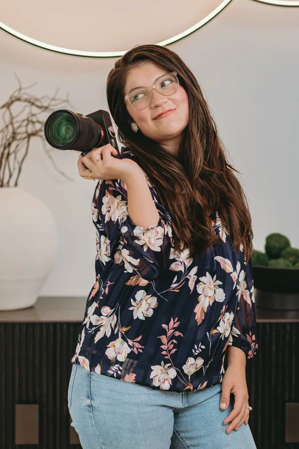 Luisa holding her camera on her shoulder with a confident, warm smile