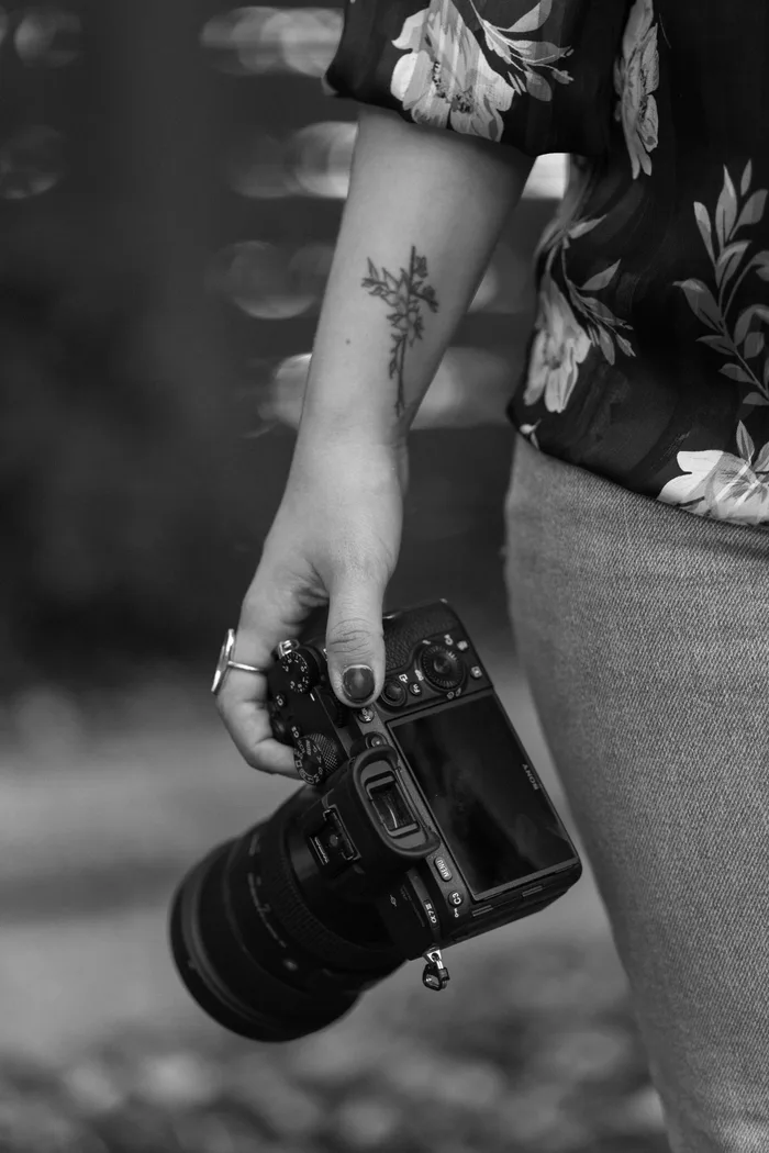 Close-up of Luisa's hand holding her camera, floral tattoo visible on her wrist